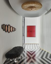 A round Murano glass
chandelier from Galerie Glustin, Paris anchors the entry passage, complementing the red hues of Pandit Khairnar’s artwork from ArtBela. An acrylic bench from Yasanche sits against a fluted curved wall adorned with antique plates from Jain Handicrafts; Photography by Suleiman Merchant