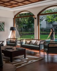 The sun dappled lounge besides the pool, layers cane, coffered ceilings and deep green upholstery creating an inviting and leisurely space; Photography by 26 : 13